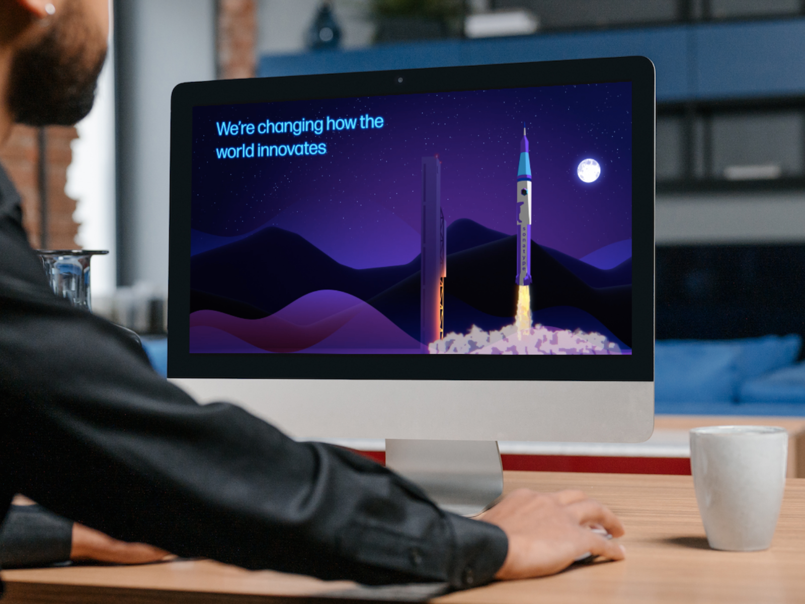 a man looks at a computer screen playing a video. The video is of a rocket ship taking off and the words"we're changing the way the world innovates" appear on screen